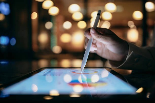 A businessperson is using a stylus to edit work reports on a tablet computer, which, combined with a mobile device, allows them to work more smoothly.
